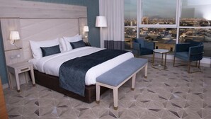 A hotel room with a large bed, bedside tables, a bench, a small table, and chairs. - RODINA (Oran)