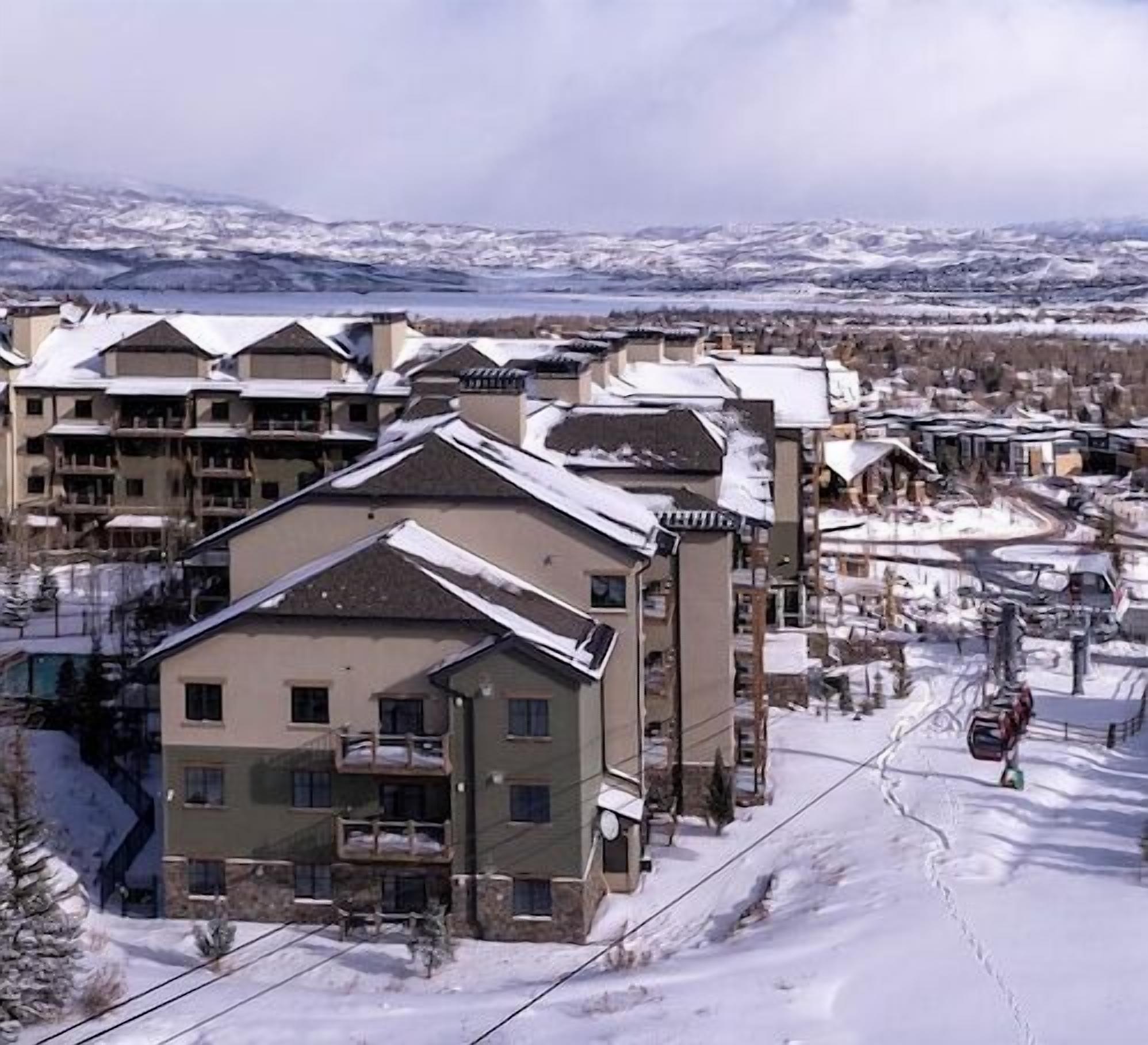 A snow-covered residential area with multi-story buildings, including a hotel with balconies and a ski lift visible in the background.