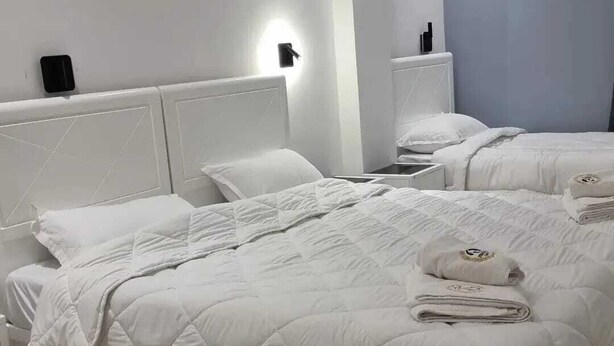 A hotel room with two beds, white bedding, a nightstand with a lamp, and a wall-mounted light. - Medina Park Hotel (Algiers)