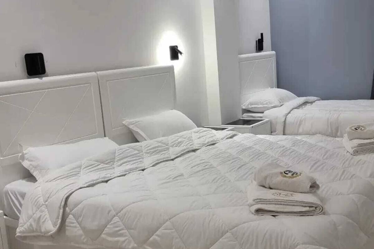 Een hotelkamer met twee bedden, wit beddengoed, een nachtkastje met lamp en een wandlamp.