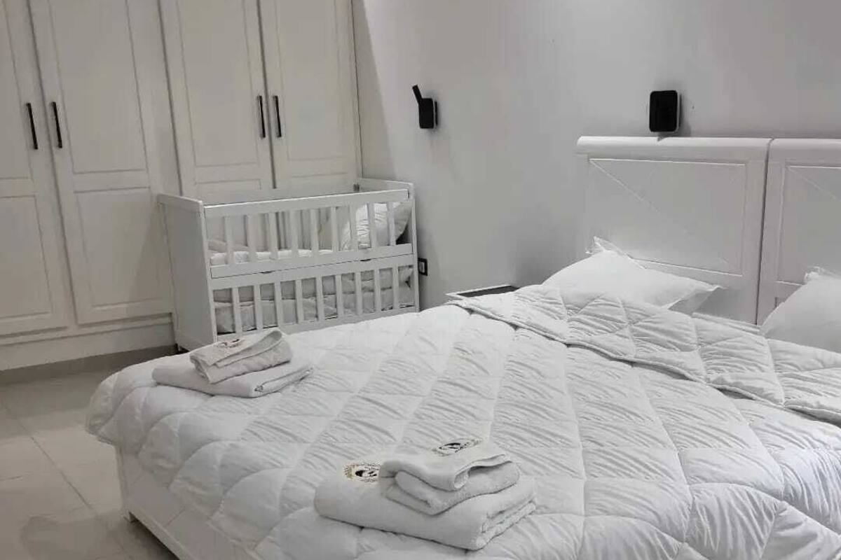 Een slaapkamer in het wit met een bed, ledikant en witte kasten.