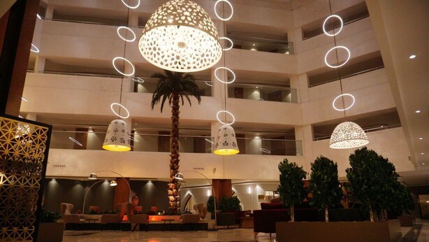 A multi-level hotel lobby with modern chandeliers, palm trees, and seating areas. - Lynatel Palace (Ouargla)