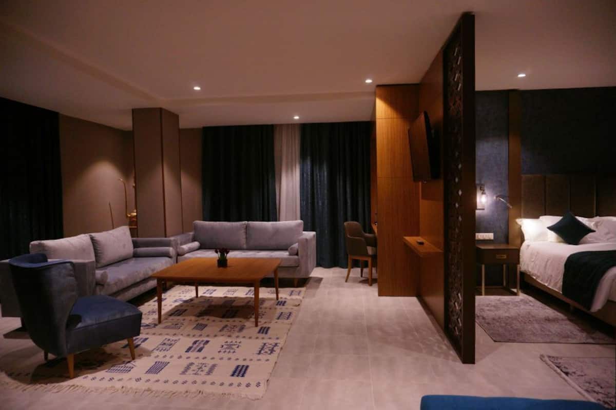 A modern hotel room with a sofa, armchair, coffee table, and a bed.