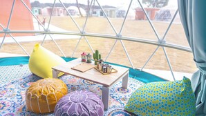 A cozy interior with a wooden table, colorful cushions, and a view through a large window.