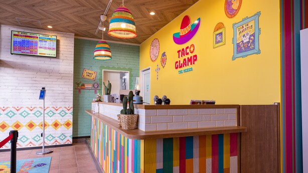 A colorful interior with a vibrant wall design, a reception desk, and a menu board.