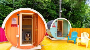 Two sauna cabins with wooden interiors, a wooden bench, and a blue and white chair outside.