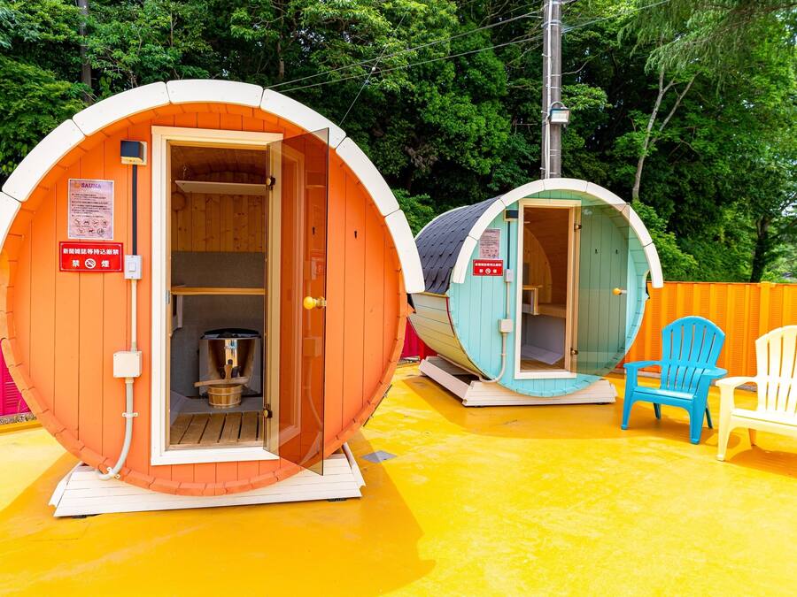 Two sauna cabins with wooden interiors, a wooden bench, and a blue and white chair outside.