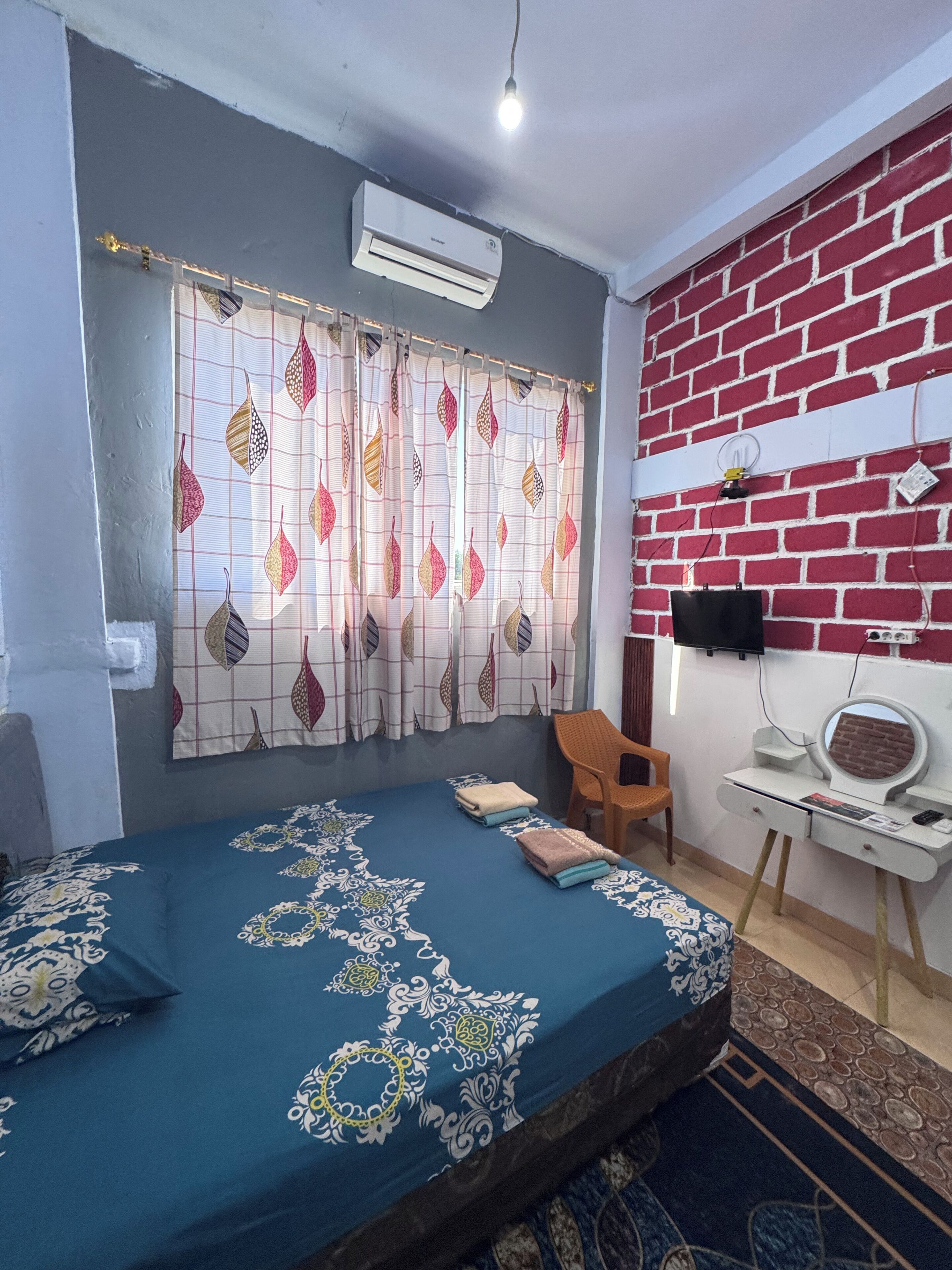 Un dormitorio con cama, escritorio, silla, aire acondicionado y pared de ladrillo.
