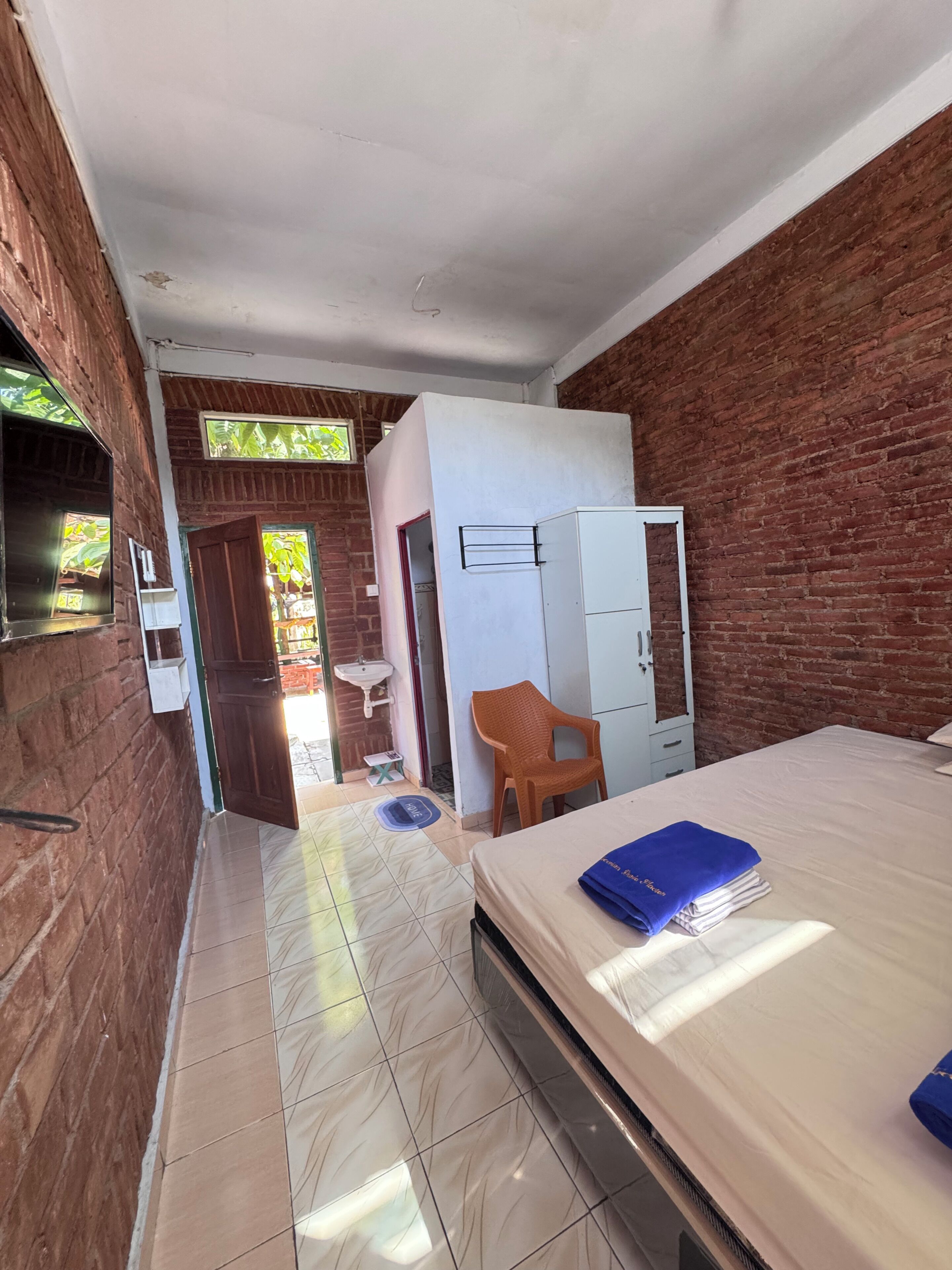 A room with a bed, a wardrobe, a sink, and a window with a view of greenery.