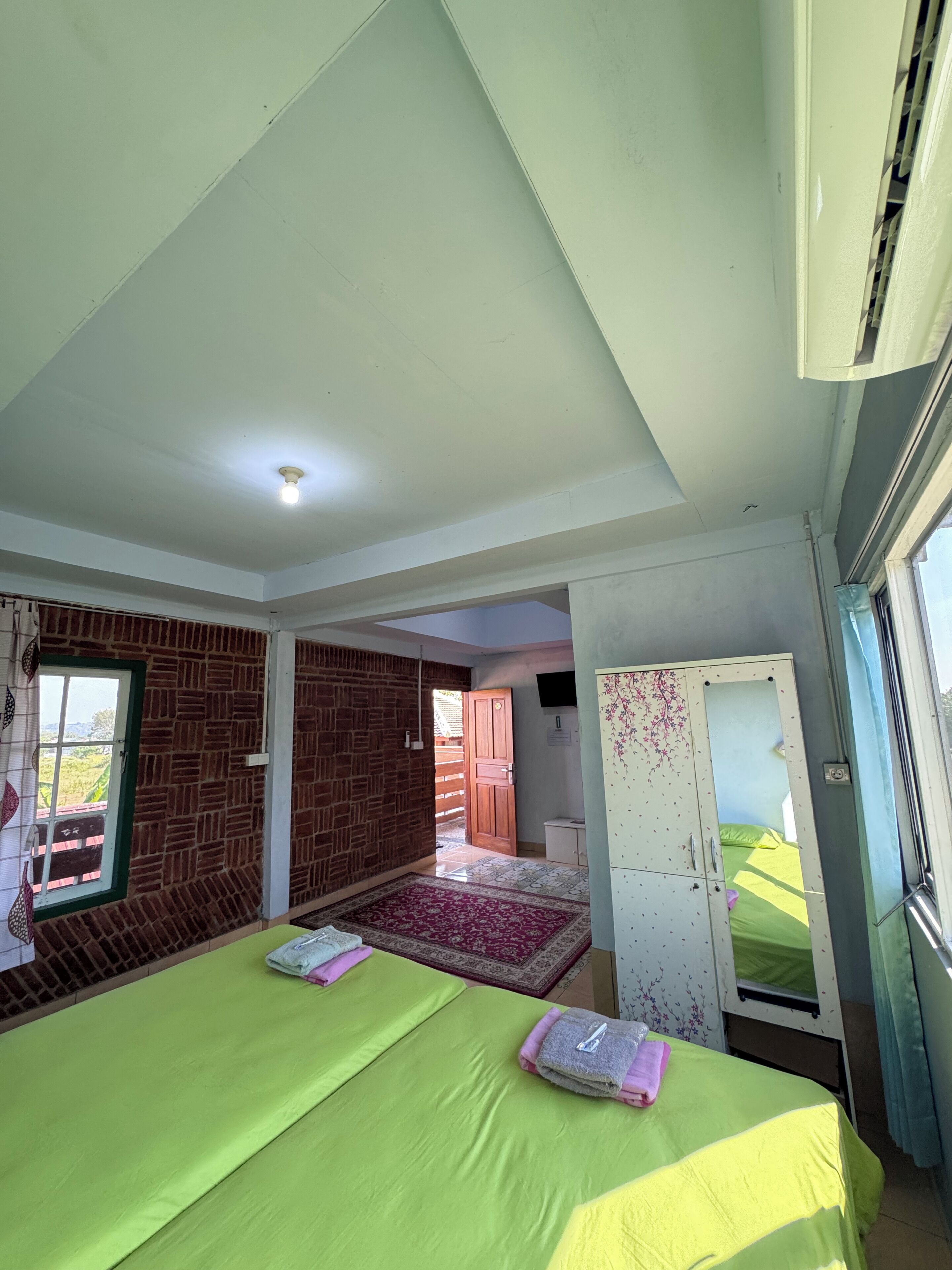 A room with two beds, a brick wall, a window, and a wardrobe.