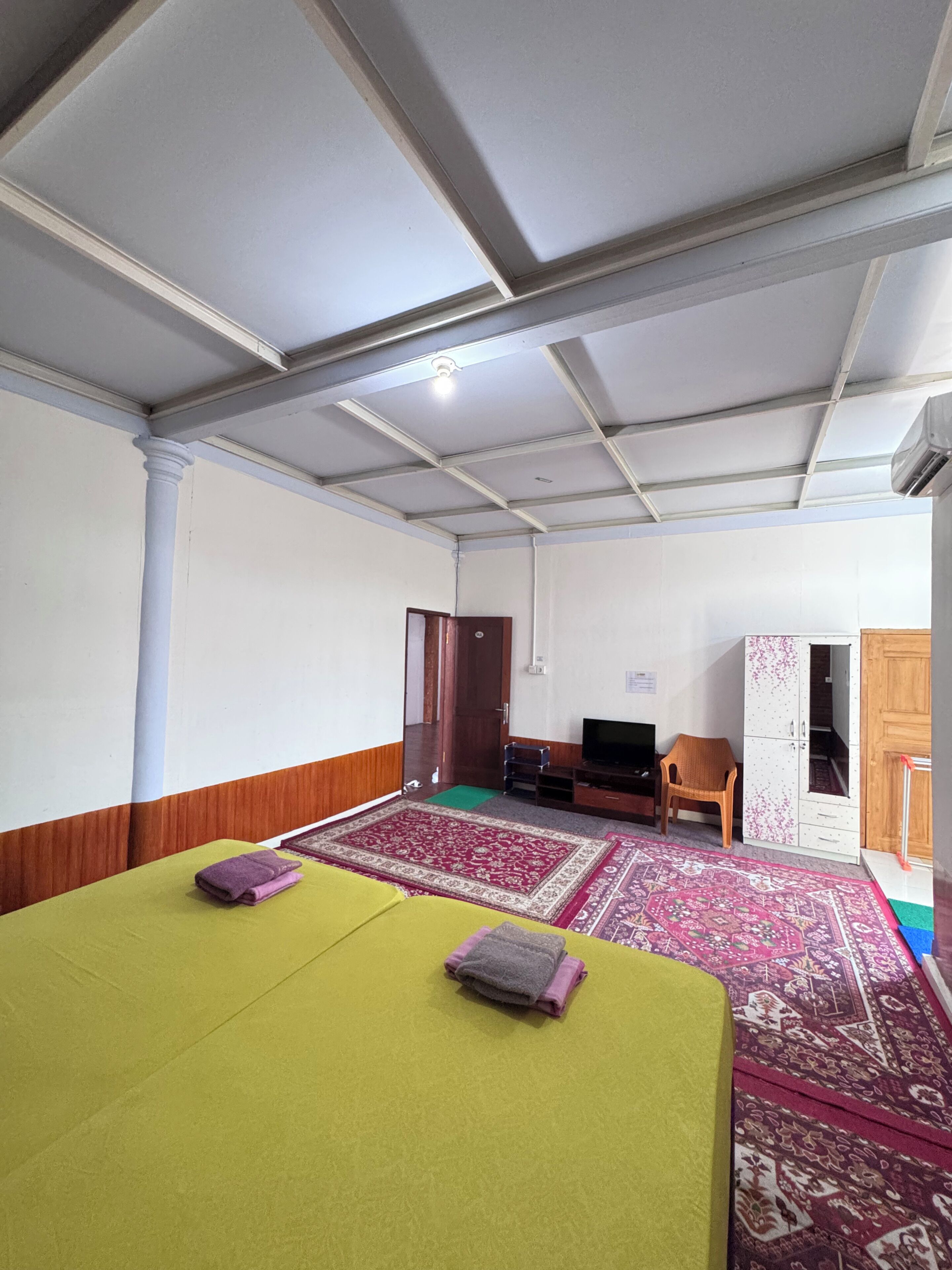 A hotel room with a bed, a television, a wardrobe, and a carpeted floor.