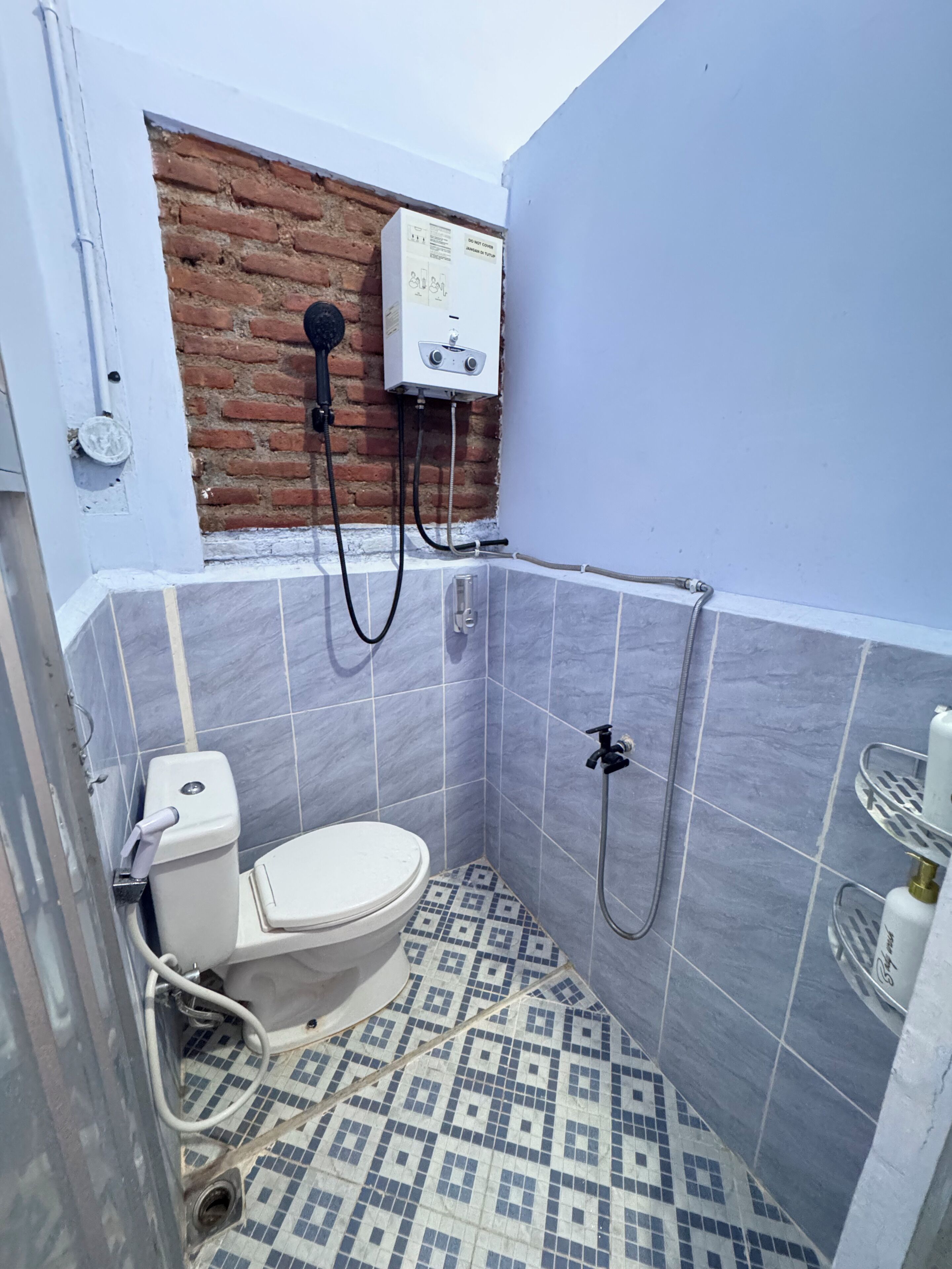 A small bathroom with a toilet, a shower, and a water heater mounted on a brick wall.