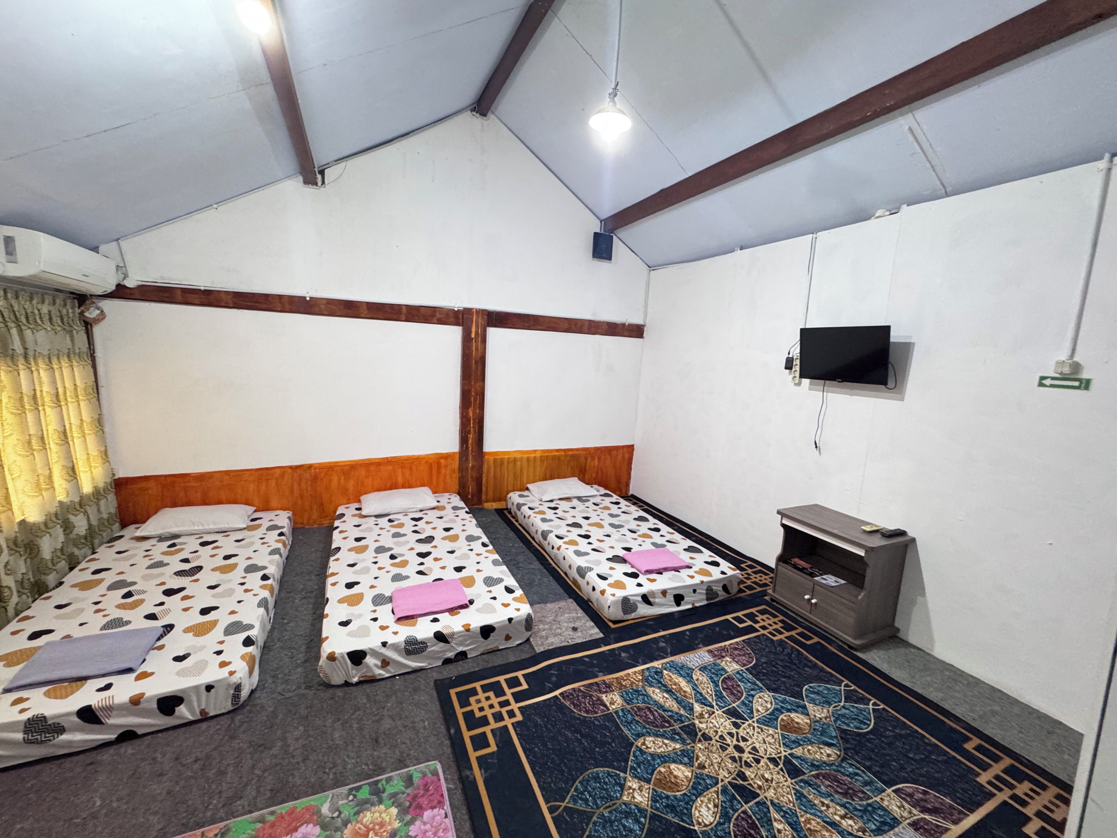 Una habitación con tres camas individuales, un televisor montado en la pared y una pequeña mesa con una silla.