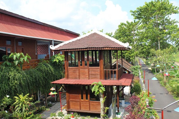 A wooden structure with a tiled roof, surrounded by lush greenery and a pathway.