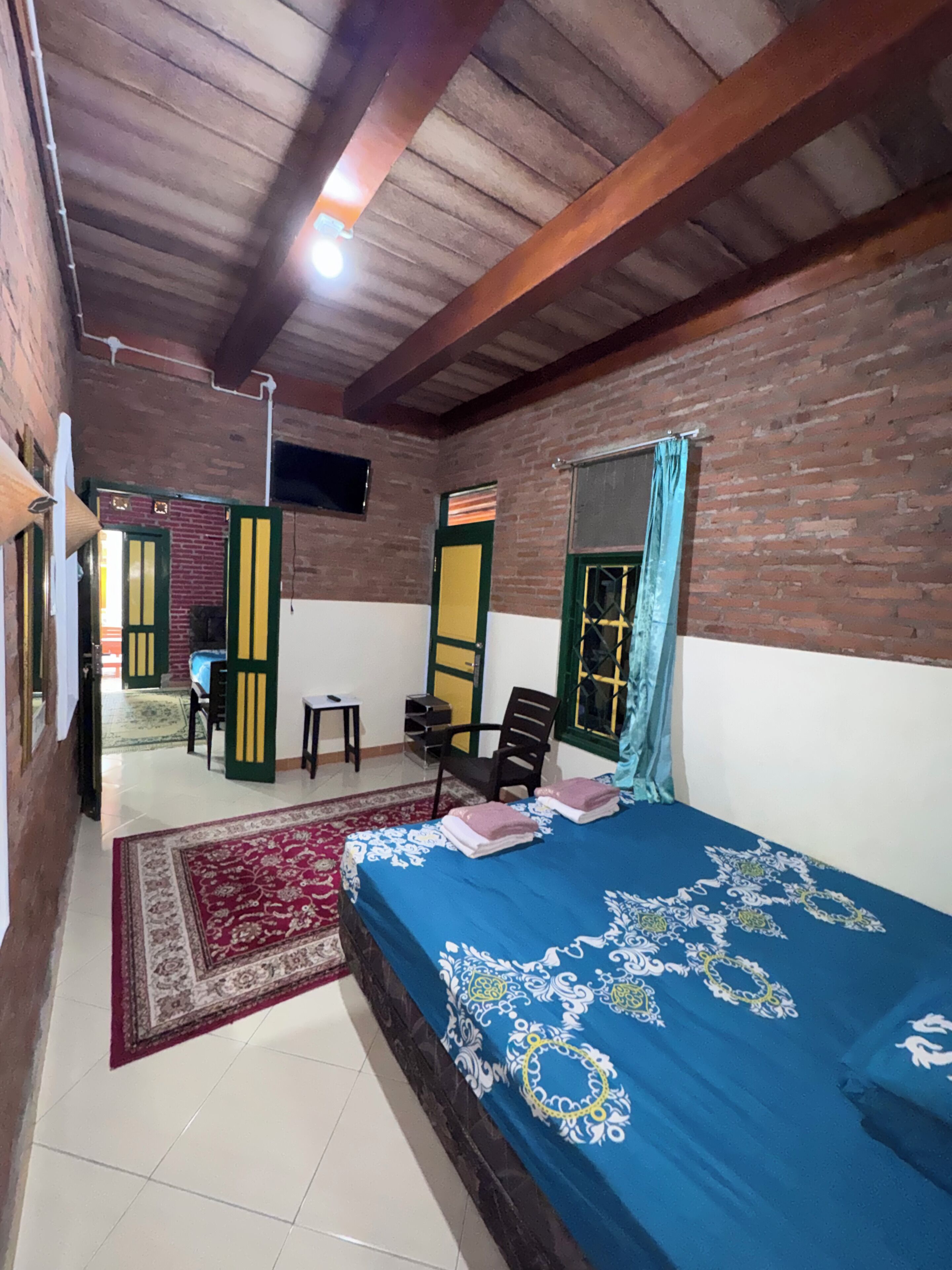 A room with a bed, a desk, and a chair. There is a window with curtains.