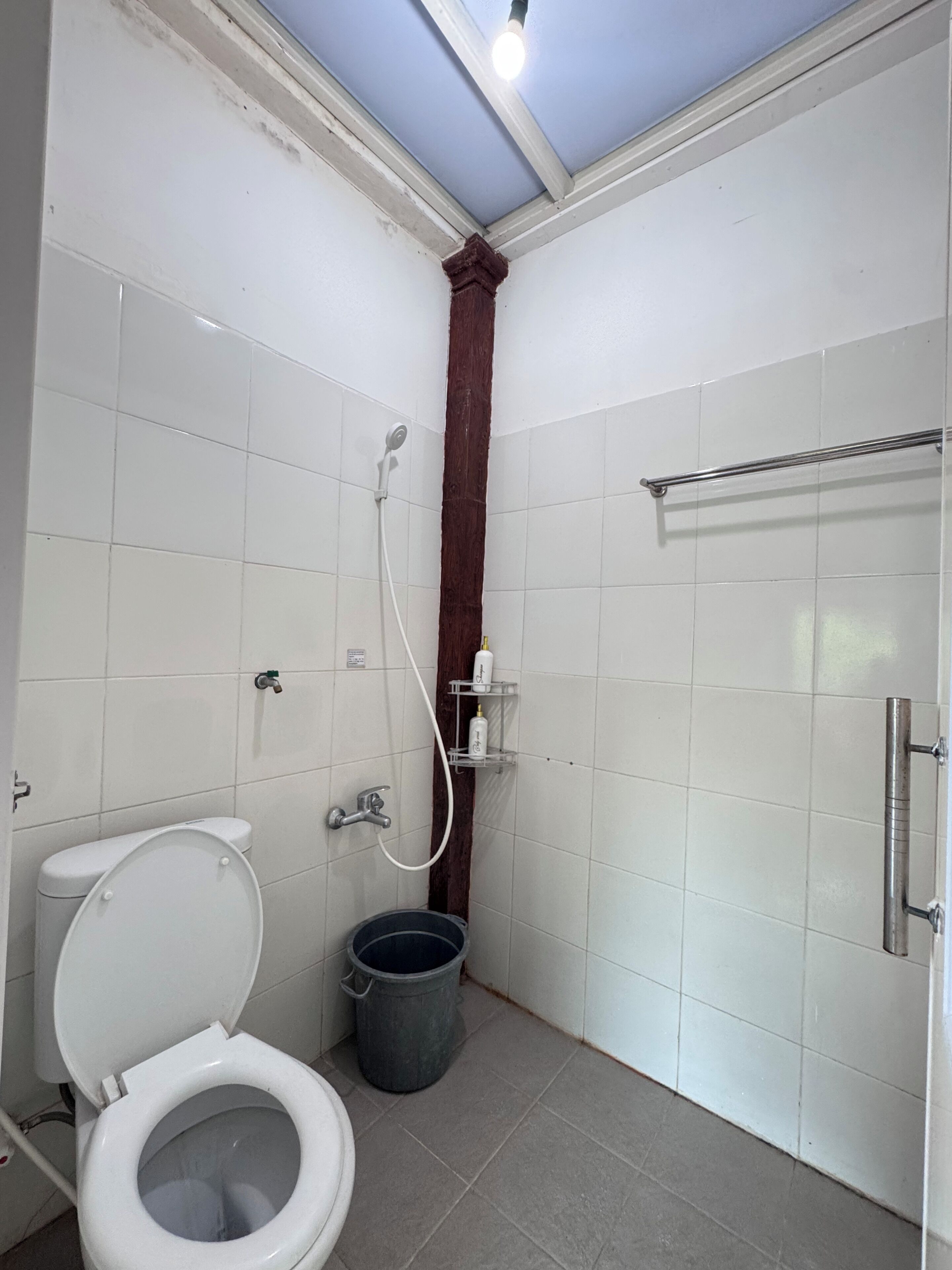 A small, compact bathroom with a toilet, shower, and a metal towel rack.