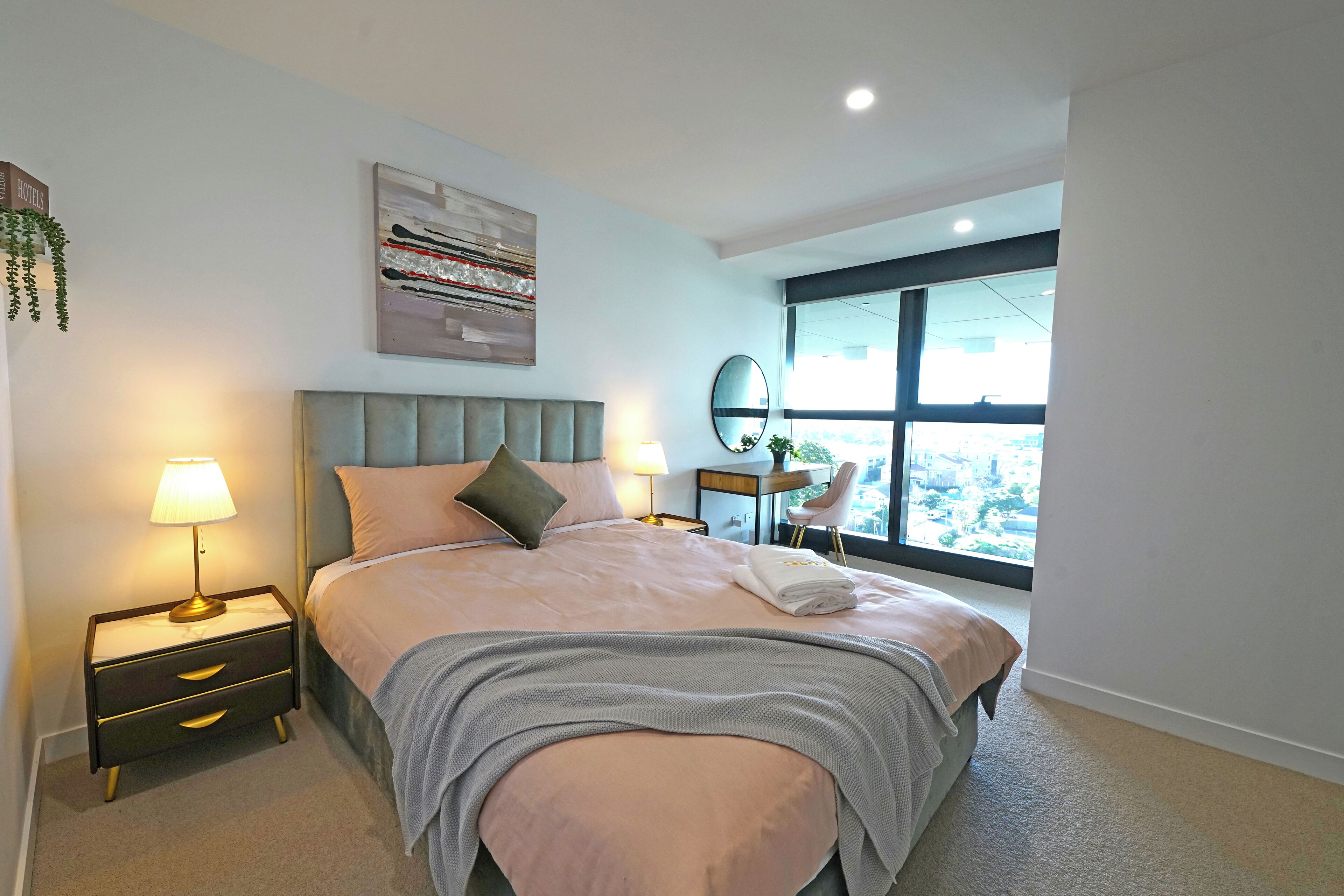 A modern hotel room with a large bed, bedside lamps, a nightstand, a mirror, and a window with a city view.
