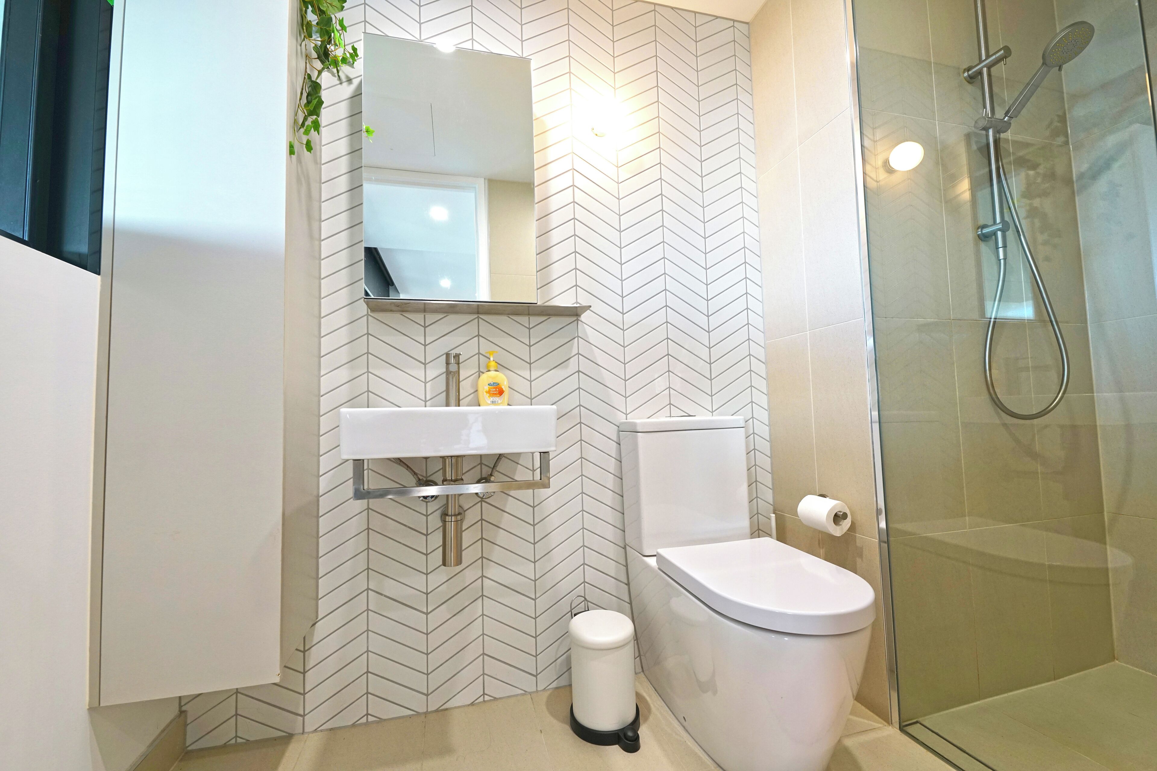 Une salle de bain moderne avec un mur recouvert de carreaux disposés en motif chevron, un lavabo blanc, des toilettes et une douche à parois de verre.