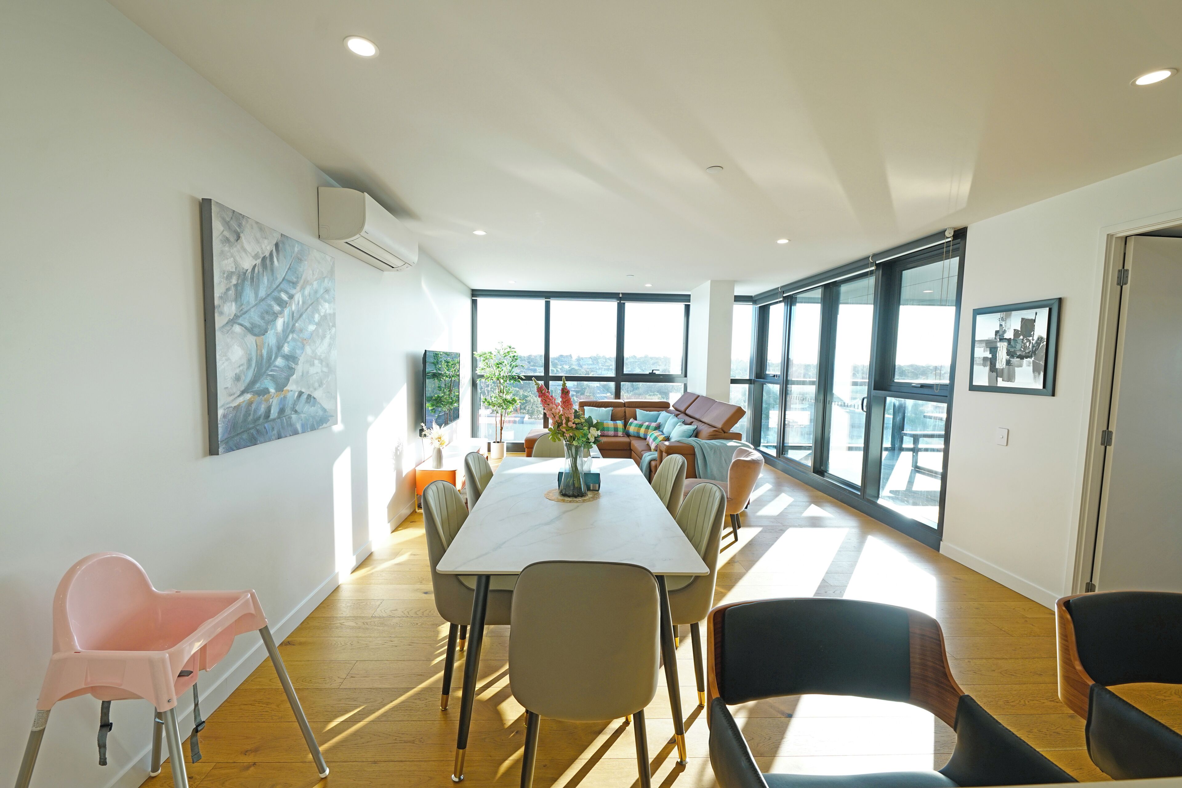 A spacious room with a large dining table, chairs, a sofa, and a view of the city through large windows.