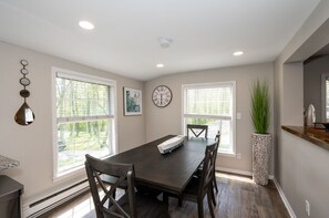 A dining room with a dark wooden table, four chairs, a clock on the wall, and large windows with blinds. - Watershed,  A River Retreat (Loveland)