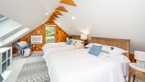 A bedroom with a sloped ceiling, wooden walls, a large bed with white bedding, a chair, a bedside table, and a window. - Watershed,  A River Retreat (Loveland)