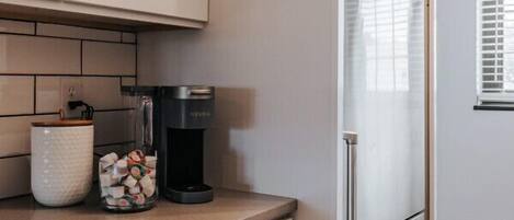 Una cocina con armarios blancos, una cafetera y un recipiente de vidrio sobre la encimera.