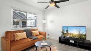 A modern living room with a sofa, a coffee table, a flat-screen TV, and a ceiling fan. - Queen Bed, Parking, Pool, Golf, Hospital, College. (Phoenix)