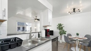 A modern kitchen with white cabinetry, a double sink, and a dining area with a round table and chairs. - Queen Bed, Parking, Pool, Golf, Hospital, College. (Phoenix)
