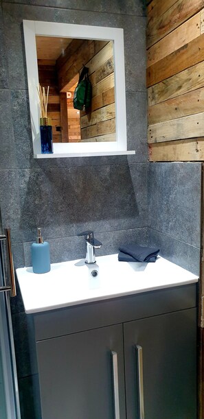 Bathroom features a white sink, chrome faucet, and mirror above a small shelf with storage.