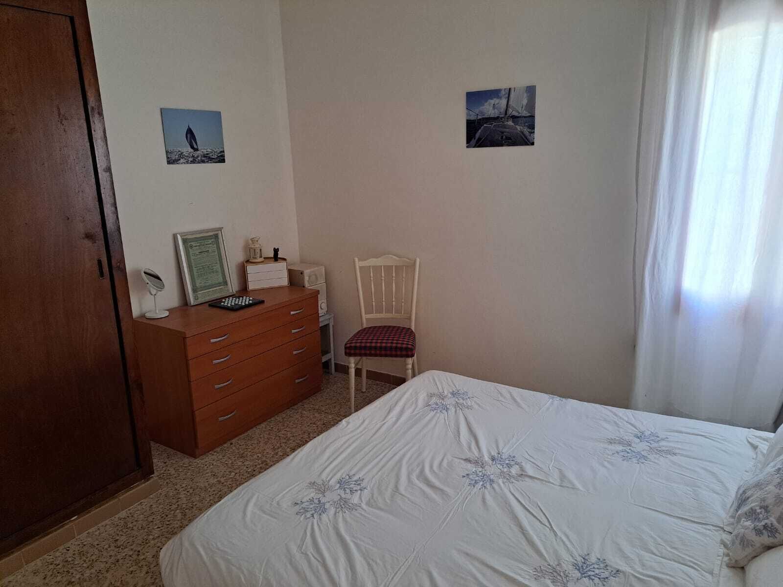 A bedroom with a bed, a wooden dresser, a chair, and two framed pictures on the wall.