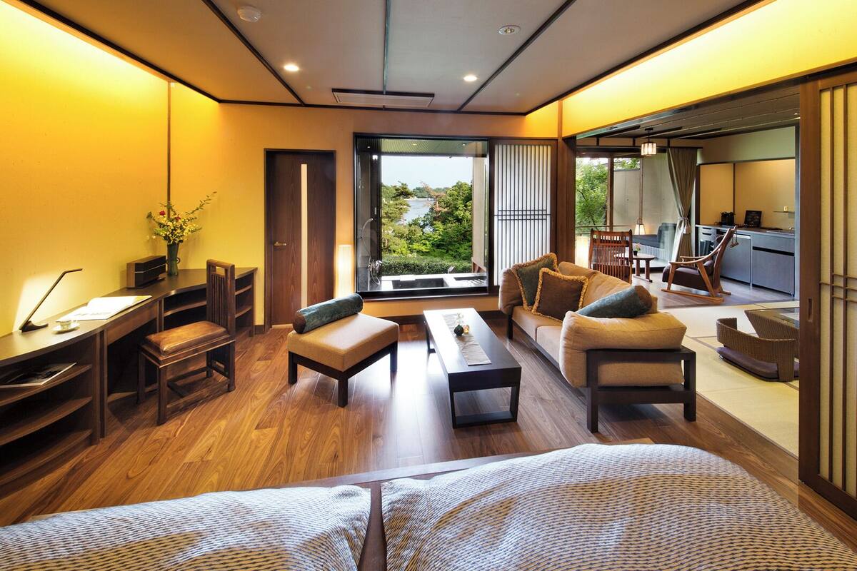 A modern hotel room with a wooden floor, a sofa, a desk, and a view of the outdoors.