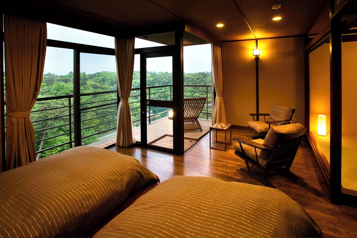 A bedroom with two beds, a balcony with a chair, and a view of a forest.