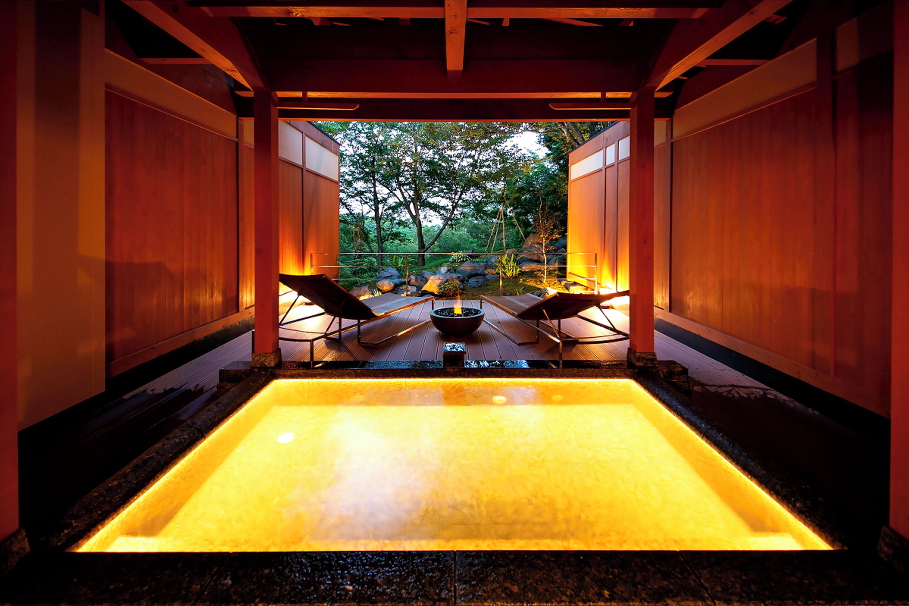 A hot spring area with a rectangular pool, wooden walls, and two lounge chairs.