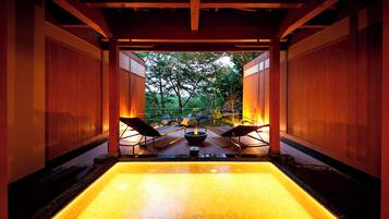 A hot spring area with a rectangular pool, wooden walls, and two lounge chairs.