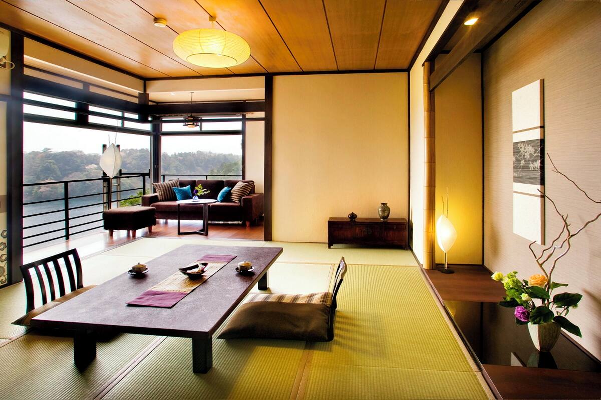 A traditional Japanese-style room with tatami flooring, a low table with cushions, a sofa, and a view of the outdoors.