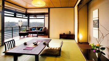A traditional Japanese-style room with tatami flooring, a low table with cushions, a sofa, and a view of the outdoors.