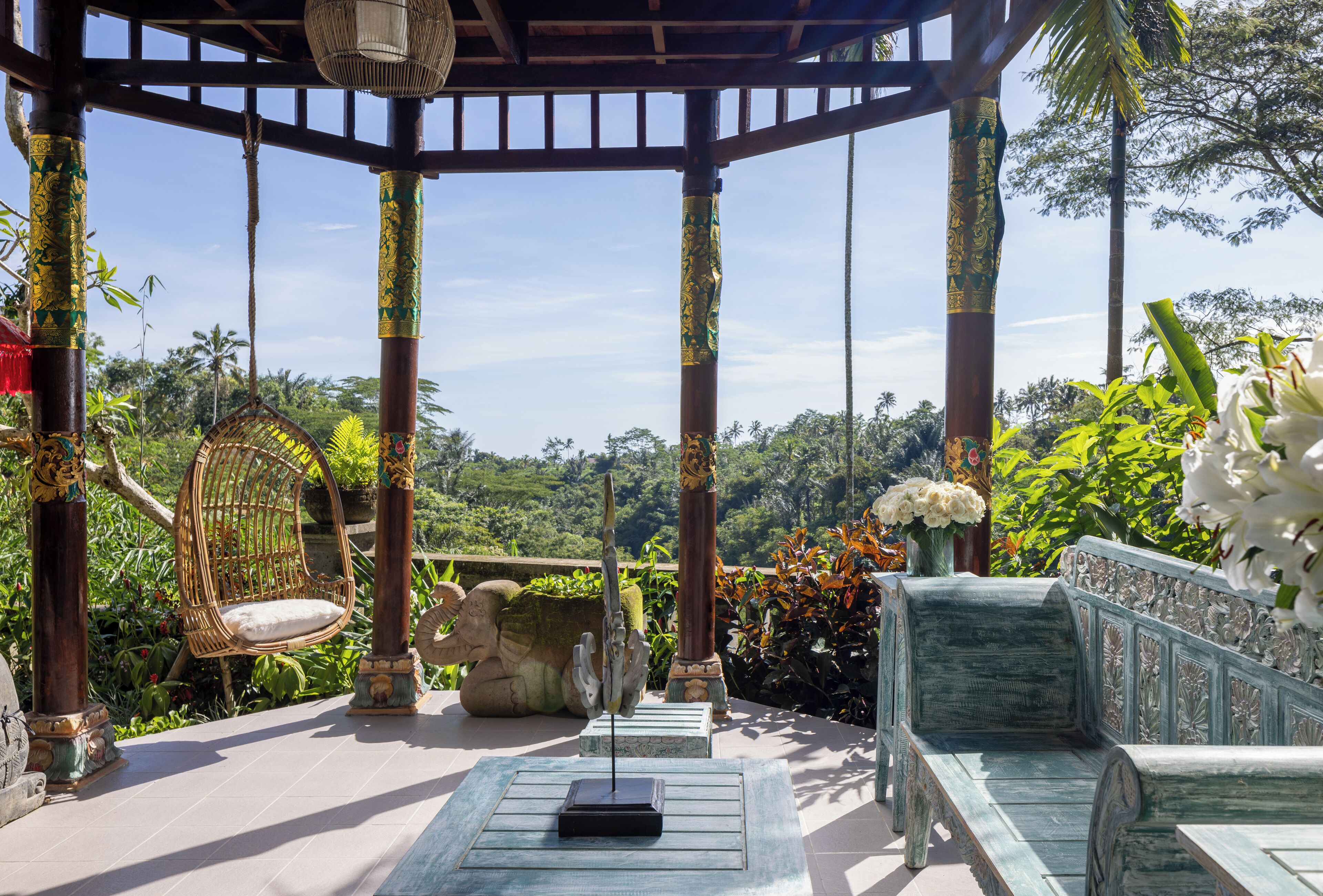 A gazebo with ornate pillars, a hanging chair, and a bench.