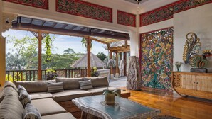A spacious room with a large sofa, a coffee table, and a decorative wall. - Villa Lembah Damai (Taro)