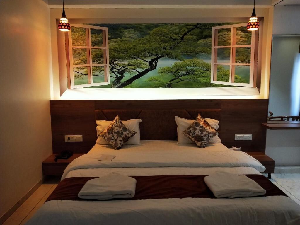 A bedroom with a large bed, two nightstands, a window with a view of trees, and two pendant lights.
