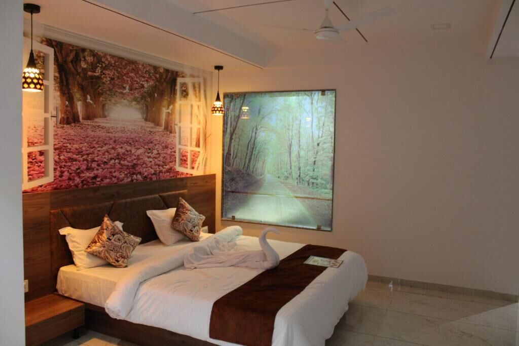 A bedroom with a bed, pillows, a blanket, a wall-mounted artwork of a forest path, and a window with a view of trees.