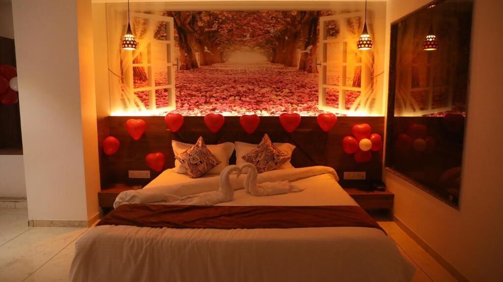 A bed with a heart-shaped pillow arrangement, a swan decoration, and a view of a rose petal-covered pathway.