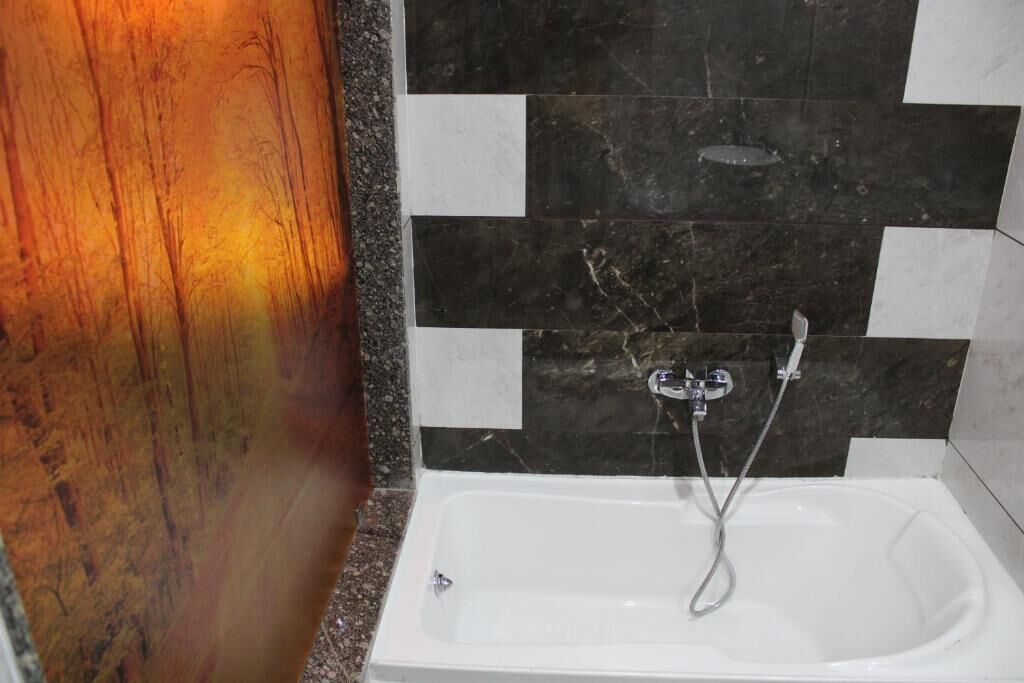 A bathroom with a white bathtub, black and white tiled walls, and a wooden panel on one side.