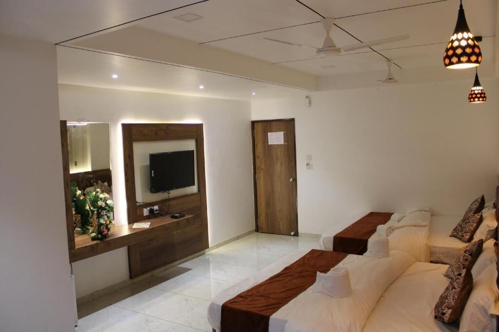 A hotel room with a large bed, a TV mounted on the wall, a wooden desk, and a mirror.