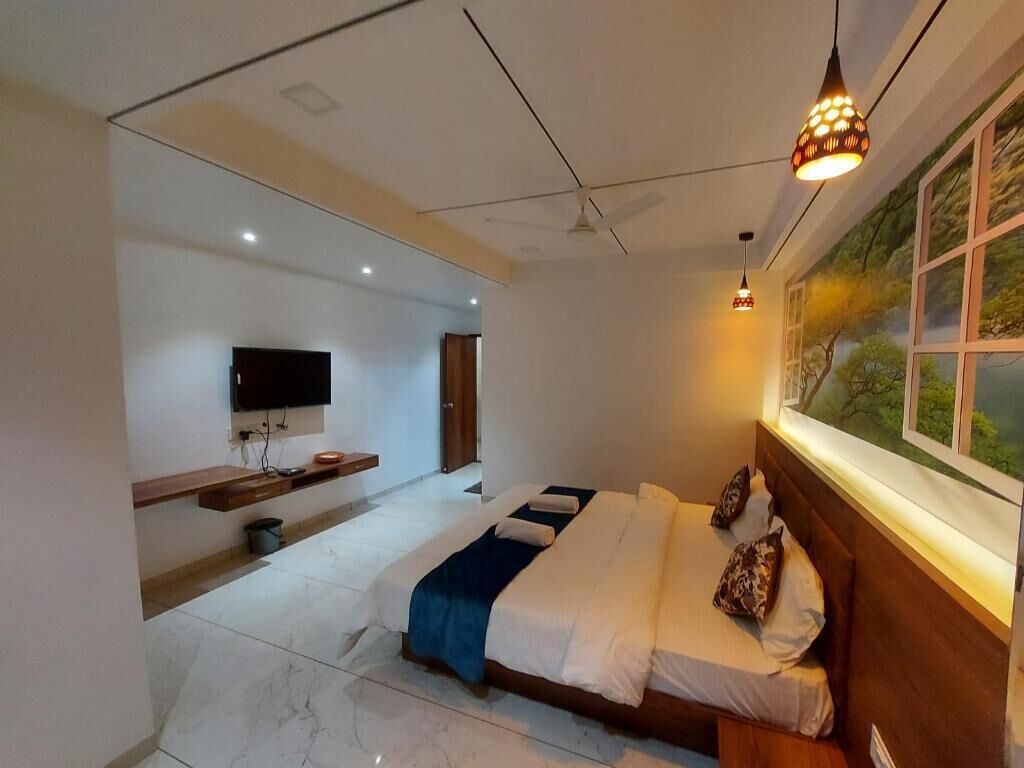 A modern bedroom with a large bed, a TV mounted on the wall, a ceiling fan, and a window with a view of trees.