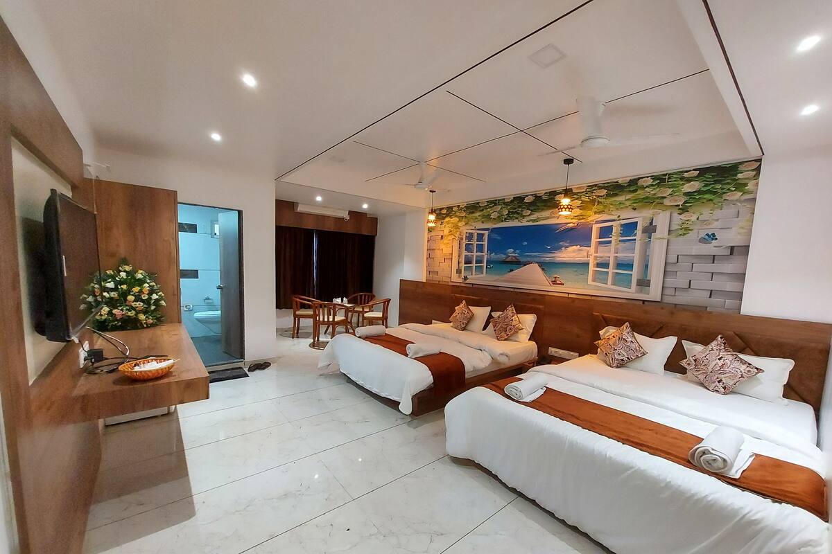 Ein modernes Hotelzimmer mit zwei Betten, einem Fernseher, einem Schreibtisch mit Lampe und einem Wandbild mit Strandmotiv.