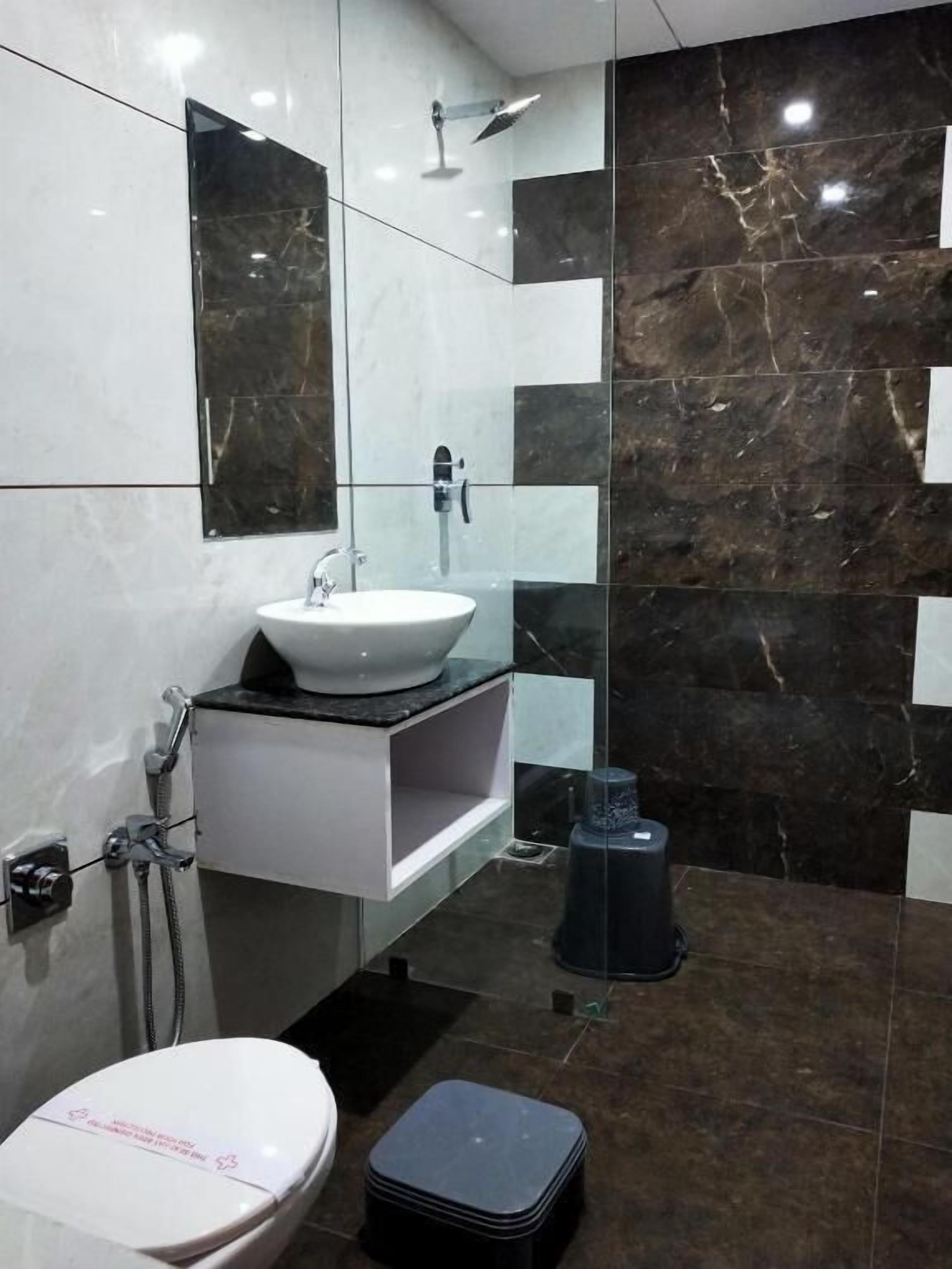 Un baño moderno con un lavamanos blanco, cabina de ducha de vidrio y un cubo de basura negro.