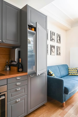A modern kitchen with grey cabinetry, a built-in wine cooler, and a blue sofa with patterned cushions. - La Maison Kléber – Luxury 1BR near Eiffel Tower & Champs-Élysées (Paris)