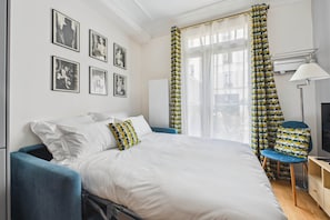 A neatly arranged hotel room with a large bed, a blue armchair, a TV, and a desk. - La Maison Kléber – Luxury 1BR near Eiffel Tower & Champs-Élysées (Paris)