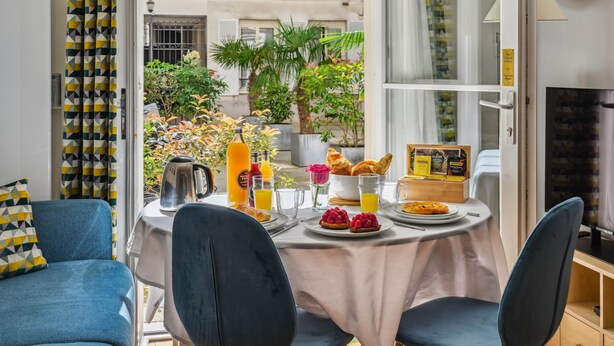 A breakfast table set with croissants, fruit, juice, and coffee, with a view of a courtyard and balcony. - La Maison Kléber – Luxury 1BR near Eiffel Tower & Champs-Élysées (Paris)