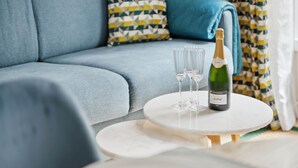 A modern living room with a blue sofa, patterned pillows, and a small white table with a bottle of champagne and glasses. - La Maison Kléber – Luxury 1BR near Eiffel Tower & Champs-Élysées (Paris)